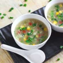 Sweet Corn Soup on a white bowl with soup spoon and garnished with some spring onions |
