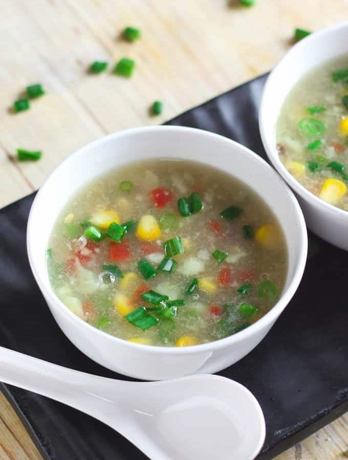 Sweet Corn Soup on a white bowl with soup spoon and garnished with some spring onions |