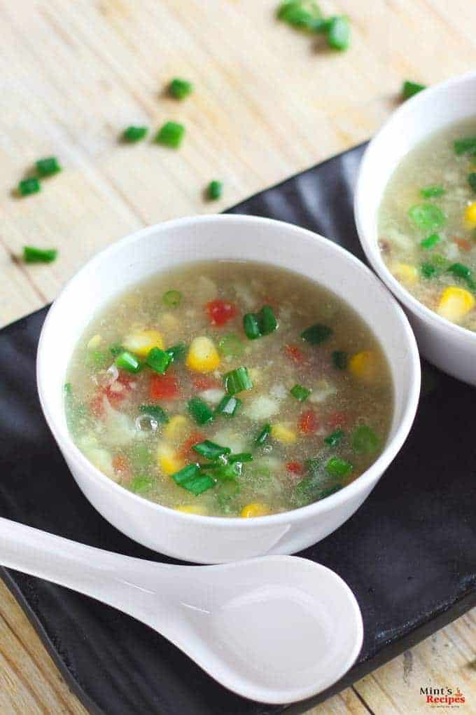 Sweet Corn Soup on a white bowl with soup spoon and garnished with some spring onions | 