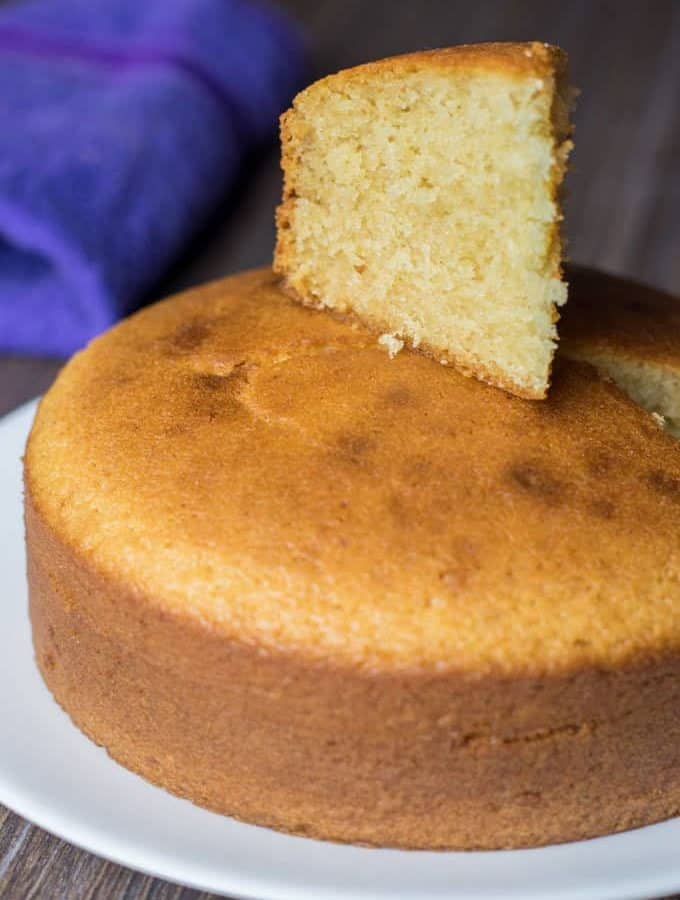 Eggless Vanilla Cake in a black plate with some gems on a white surface |