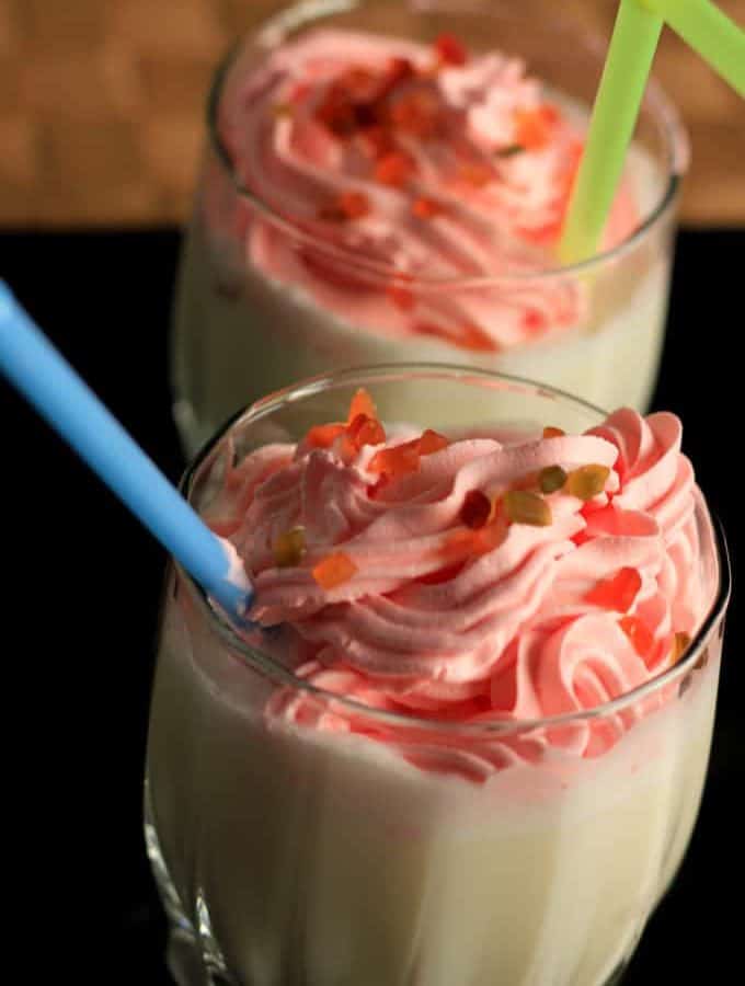 Vanilla milkshake on glass with some tutti fruity sprinkles on it with a strow on a dark background |