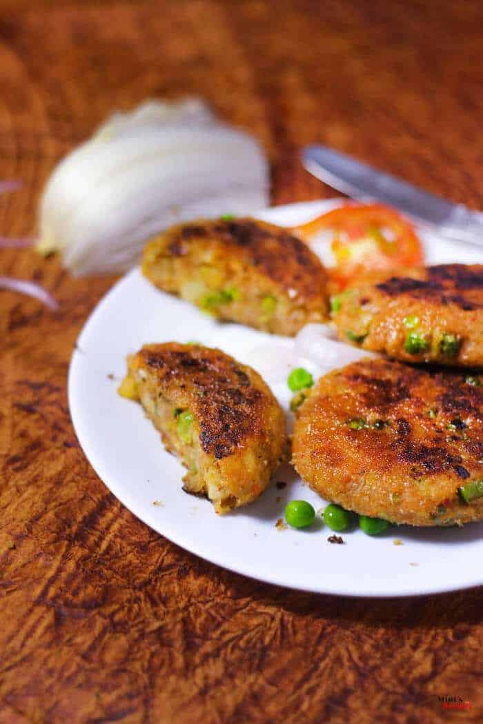 Veg Aloo Tikki on a white plate with some aloo tikki and garnished with some green peas kept on dark color paper surface 