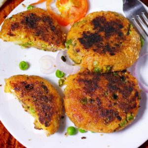 Veg Aloo Tikki on a white plate with some aloo tikki and garnished with some green peas kept on dark color paper surface