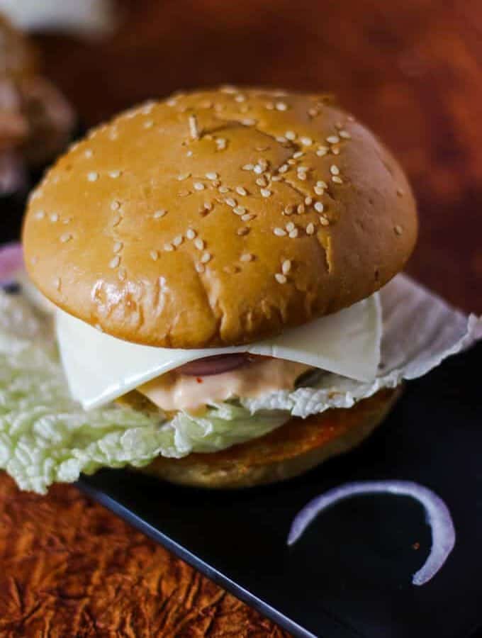Vegetable Burgers on a black rectangular tray with some onion slices kept on a dark paper surface with dark background |