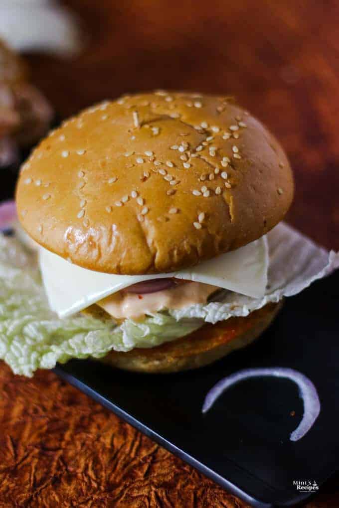 Vegetable Burgers on a black rectangular tray with some onion slices kept on a dark paper surface with dark background |