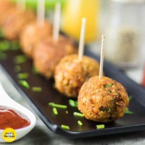 Veg Kurkure Lollipops on a white tray with some green chutney and tomato ketchup dips on the bckground and decorated with some coriander leaves and cornflakes|