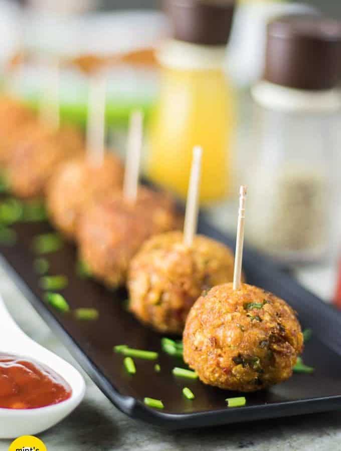 Veg Kurkure Lollipops on a white tray with some green chutney and tomato ketchup dips on the bckground and decorated with some coriander leaves and cornflakes|