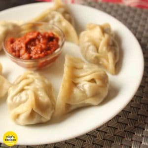 Veg momos on a white plate with some red chilli sauce