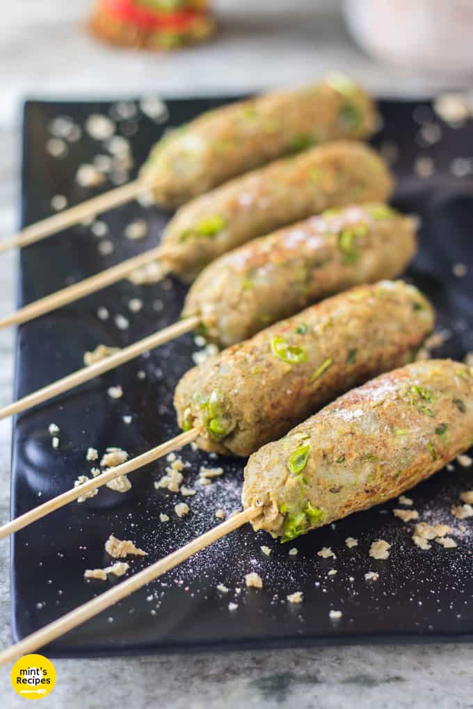 Veg Soya Kebab on a black tray with some green peas on the surface and some wooden pots in the background