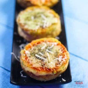 Veg Suji Buns on a black tray with some suji buns garnished with some cheese and oregano kept on a wooden surface |