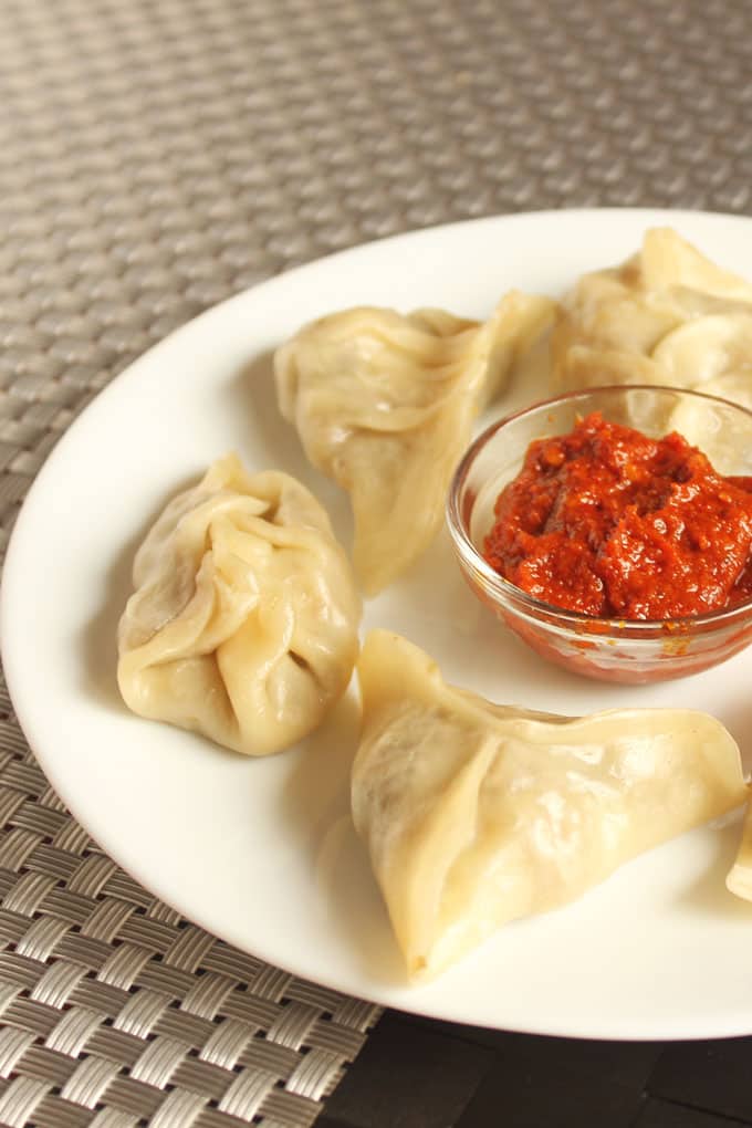 Veg momos on a white plate with some red chilli sauce 