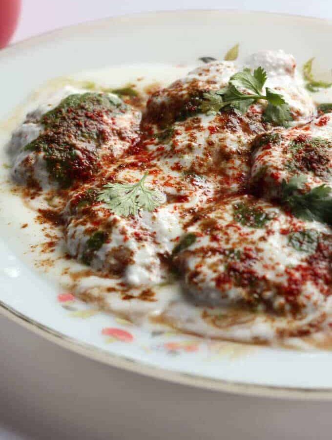 Dahi Vada on a white plate garnished with red chilli powder coriander leaves little chaat masala