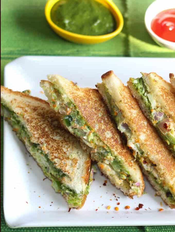 Veg Mayonnaise Sandwich Recipe on a white tray with chilli flakes and some green chutney and tomato ketchup on the background |